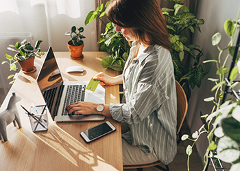 woman typing on laptop while holding a credit card