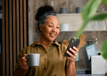 woman drinking from a mug while looking at her phone
