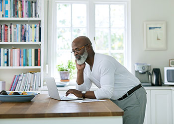 man leaning over counter working on laptop