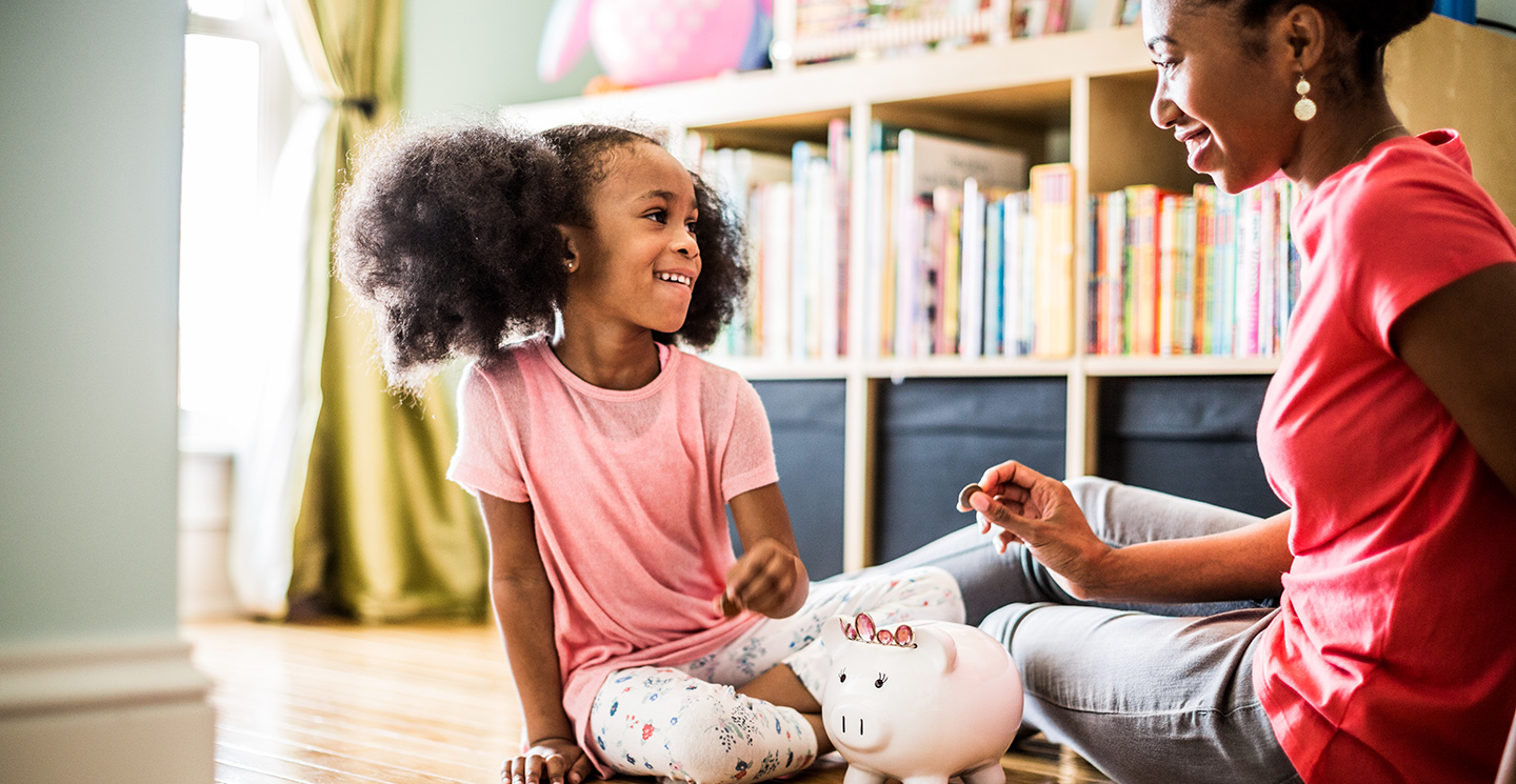 mom and daughter adding money to piggy bank